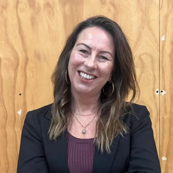 Woman smiling in black blazer against wooden wall background